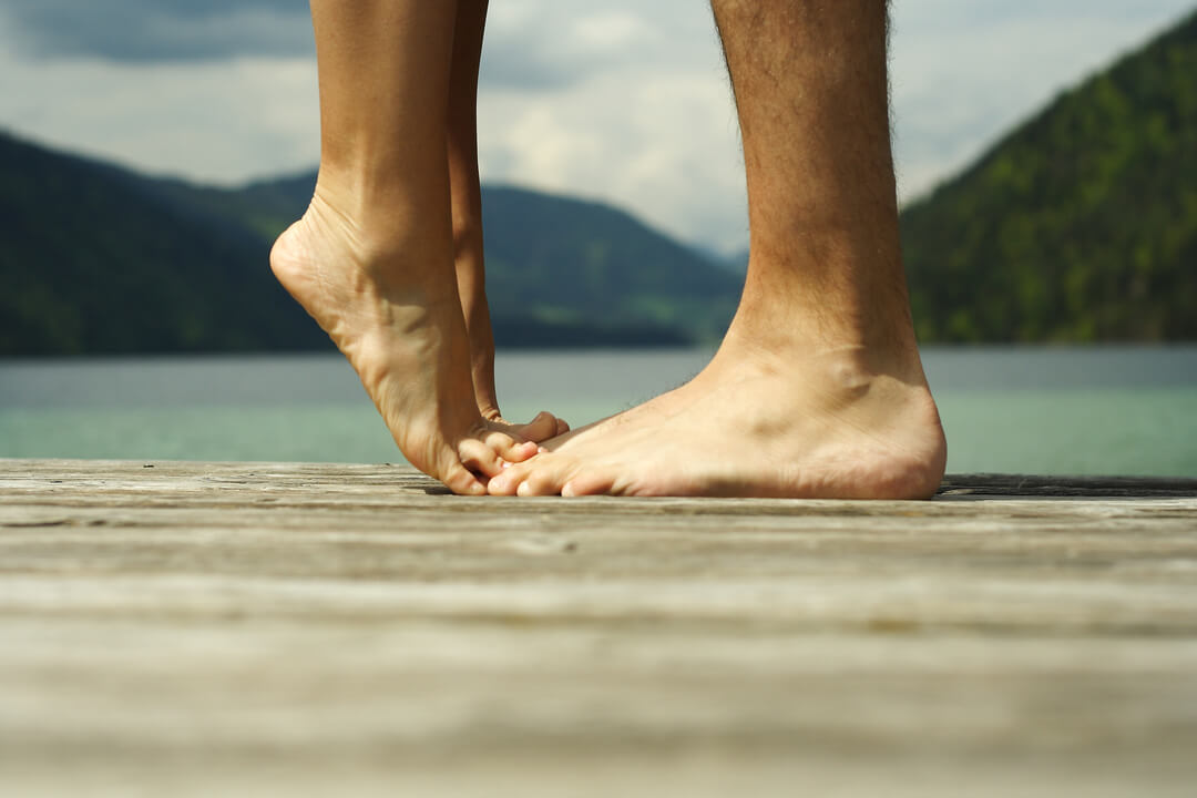 Cuidados com os pés: mulher na ponta do pé ao lado de homem em um píer ao ar livre.