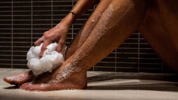 Mulher no banho, esfregando as pernas em sua rotina de cuidados com os pés.